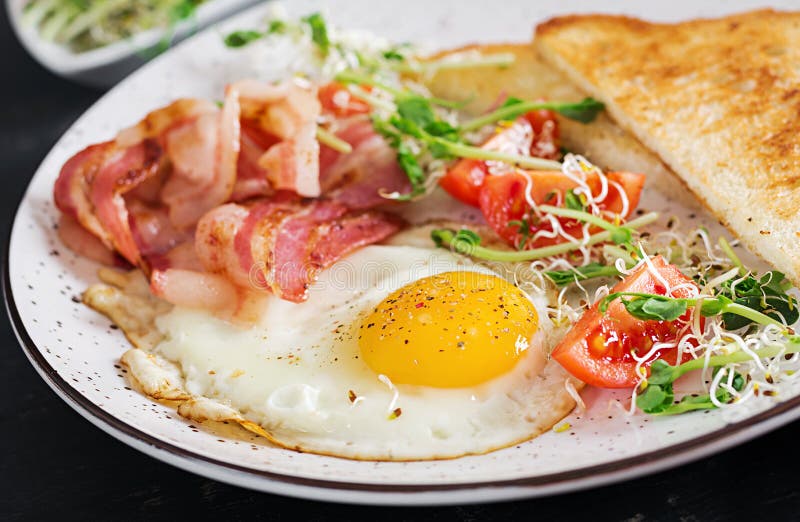 Prima colazione inglese - pane tostato, uovo, bacon e pomodori ed insalata dei microgreens