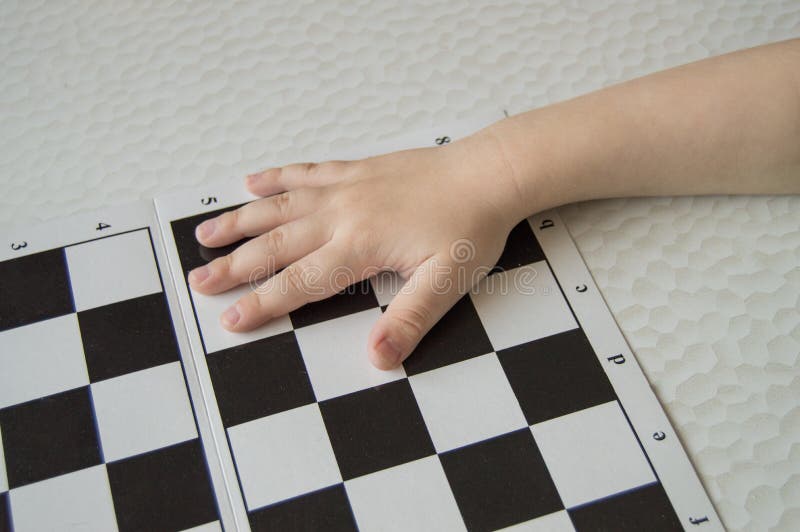 Primer de la mano de un pequeño niño que miente en el tablero de ajedrez, el concepto de aprendizaje y el desarrollo intelectual imagen de archivo Primer de la mano de un pequeño niño que miente en el tablero de ajedrez, el concepto de aprendizaje y el desarrollo intelectual imagen de archivo