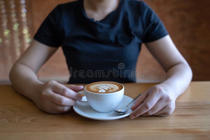 Primer de la mujer joven de las manos que sostiene una taza de café en un café foto de archivo