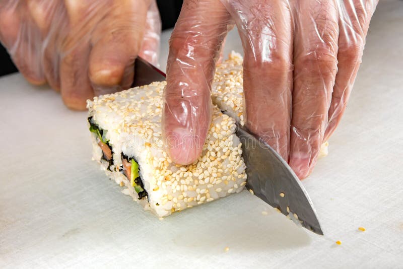 Primer de las manos del cocinero que ruedan encima de cortes del sushi en porciones en cocina foto de archivo libre de regalías Primer de las manos del cocinero que ruedan encima de cortes del sushi en porciones en cocina foto de archivo libre de regalías