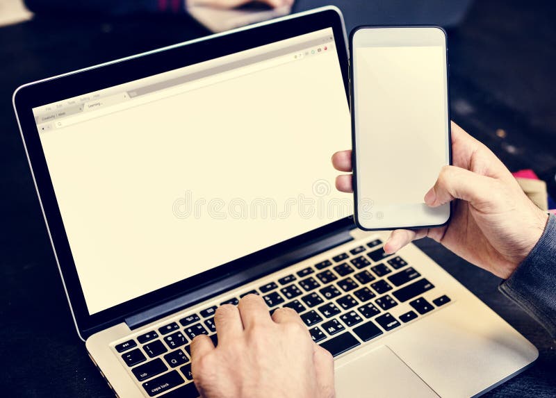 Primer de las manos que sostienen el teléfono móvil con el fondo del ordenador portátil del ordenador fotografía de archivo libre de regalías Primer de las manos que sostienen el teléfono móvil con el fondo del ordenador portátil del ordenador fotografía de archivo libre de regalías