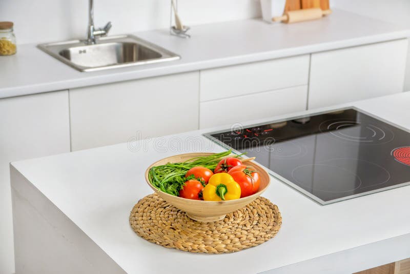 Primer de las verduras en el cuenco en cocina blanca moderna con la inducción que cocinan el calentador y el fregadero en fondo fotografía de archivo Primer de las verduras en el cuenco en cocina blanca moderna con la inducción que cocinan el calentador y el fregadero en fondo fotografía de archivo