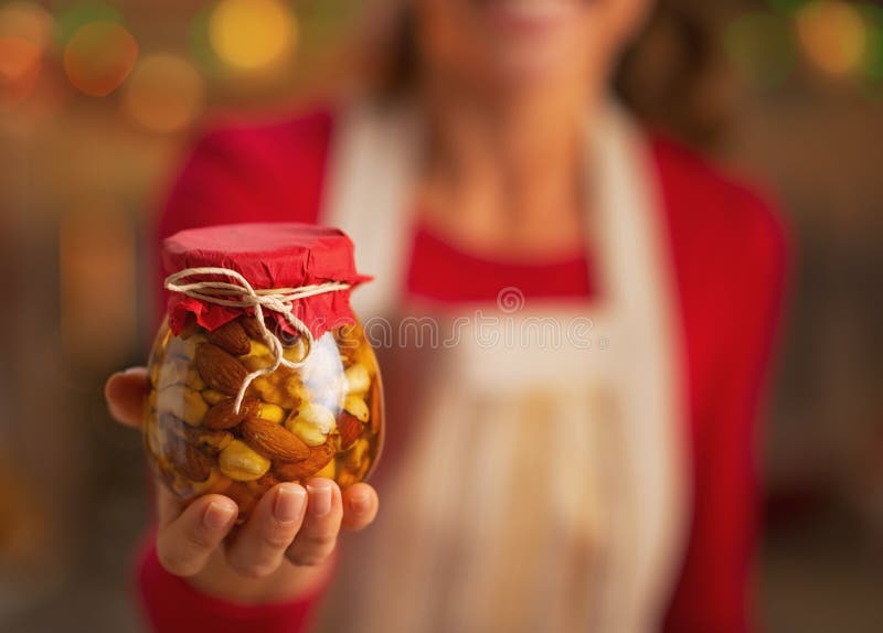 Primer en el ama de casa joven que muestra el tarro con las nueces de la miel imágenes de archivo libres de regalías Primer en el ama de casa joven que muestra el tarro con las nueces de la miel imágenes de archivo libres de regalías