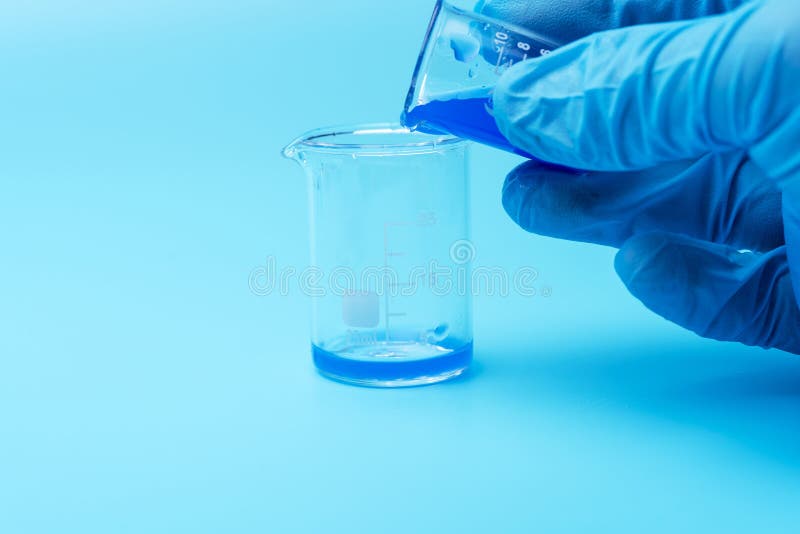 Primer en las manos de un científico que lleva guantes de goma azules y que vierte las sustancias químicas líquidas del vidrio al foto de archivo Primer en las manos de un científico que lleva guantes de goma azules y que vierte las sustancias químicas líquidas del vidrio al foto de archivo