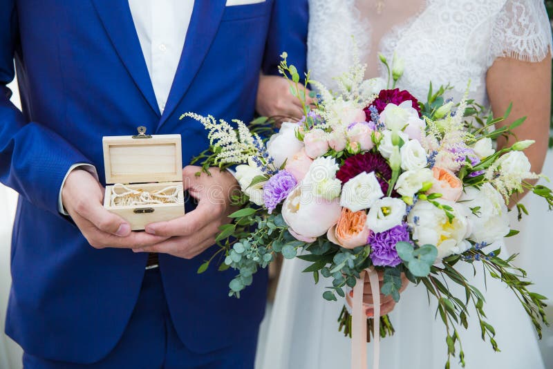 Primer Manos de la novia y del novio que sostienen el ramo y caja con los anillos en ataúd fotografía de archivo libre de regalías Primer Manos de la novia y del novio que sostienen el ramo y caja con los anillos en ataúd fotografía de archivo libre de regalías