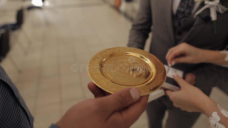 Primer plano de los anillos de boda de los recién casados en placa de oro con agua bendita durante la ceremonia del matrimonio