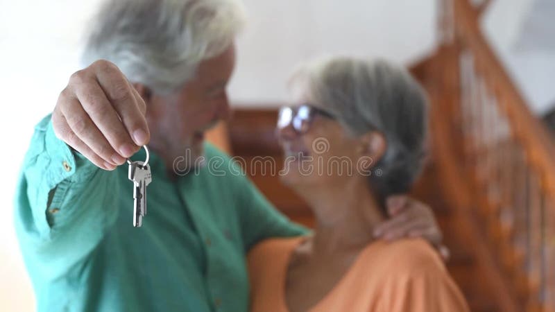 Primer plano de mujer y hombre mayores y maduros en casa sosteniendo llaves de casa a la cámara. retrato de pareja de senior sonri almacen de metraje de vídeo