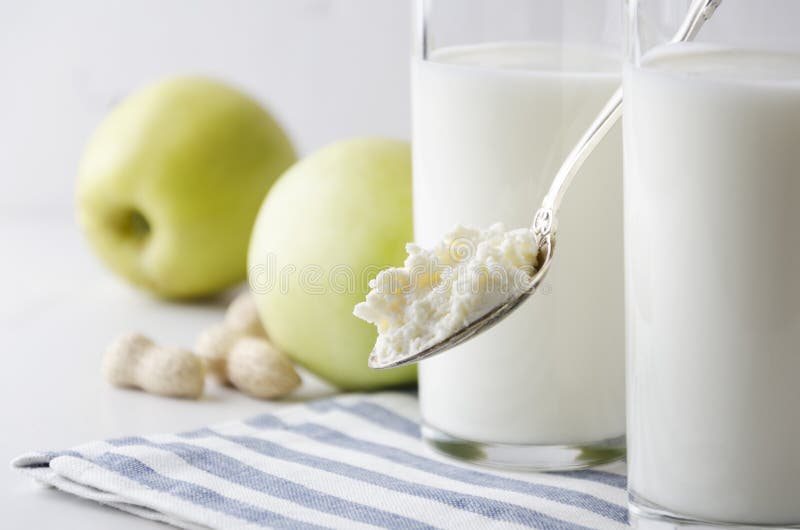 Primo piano del cucchiaio con la ricotta contro i bicchieri di latte, mela, dadi Concetto dello stile di vita sano, alimento salu fotografie stock libere da diritti Primo piano del cucchiaio con la ricotta contro i bicchieri di latte, mela, dadi Concetto dello stile di vita sano, alimento salu fotografie stock libere da diritti