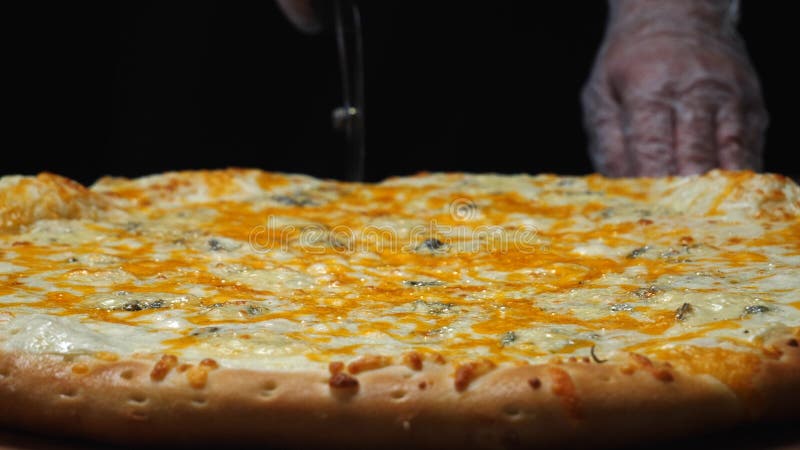Primo piano del cuoco unico in guanti bianchi che tagliano la pizza di formaggio deliziosa quattro sul bordo di legno sulla tavol fotografia stock libera da diritti Primo piano del cuoco unico in guanti bianchi che tagliano la pizza di formaggio deliziosa quattro sul bordo di legno sulla tavol fotografia stock libera da diritti