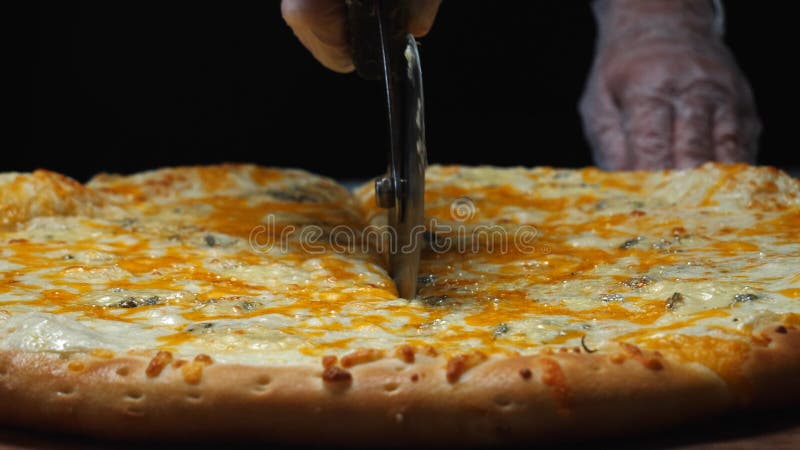 Primo piano del cuoco unico in guanti bianchi che tagliano la pizza di formaggio deliziosa quattro sul bordo di legno sulla tavol fotografie stock libere da diritti Primo piano del cuoco unico in guanti bianchi che tagliano la pizza di formaggio deliziosa quattro sul bordo di legno sulla tavol fotografie stock libere da diritti