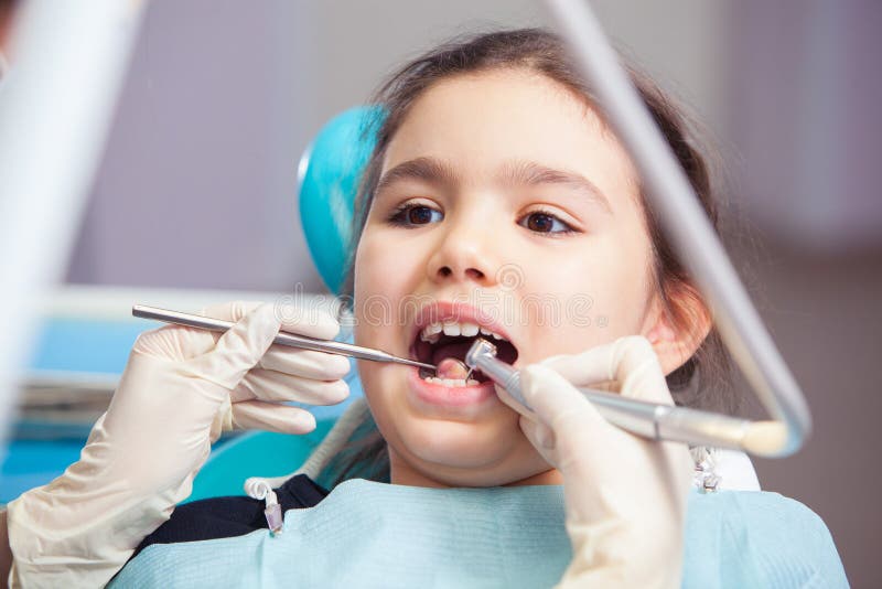 Primo piano della bambina graziosa che apre il suo bocca largamente durante il trattamento dei suoi denti dal dentista fotografie stock libere da diritti Primo piano della bambina graziosa che apre il suo bocca largamente durante il trattamento dei suoi denti dal dentista fotografie stock libere da diritti
