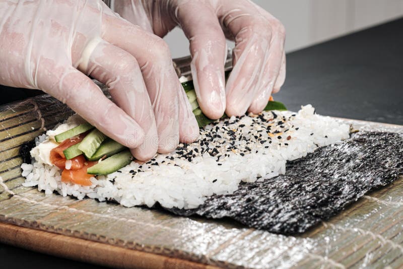 Primo piano delle mani del cuoco Un cuoco unico maschio fa i sushi ed i rotoli da riso, dal pesce rosso e dall'avocado Guanti bia immagine stock libera da diritti