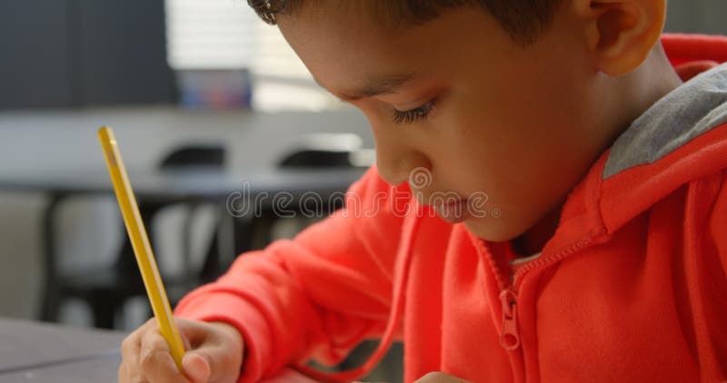 Primo piano dello scolaro asiatico attento che studia allo scrittorio in aula alla scuola 4k