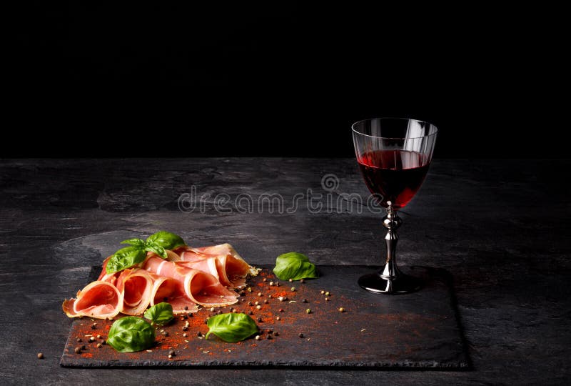 Primo piano di una composizione della gastronomie Un vetro di vino, un prosciutto di Parma e le foglie pieni del basilico su un f fotografia stock Primo piano di una composizione della gastronomie Un vetro di vino, un prosciutto di Parma e le foglie pieni del basilico su un f fotografia stock