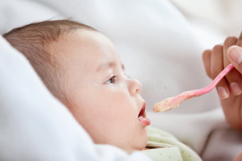 Primo piano di una madre che dà alimento al suo bambino sveglio immagini stock libere da diritti Primo piano di una madre che dà alimento al suo bambino sveglio immagini stock libere da diritti