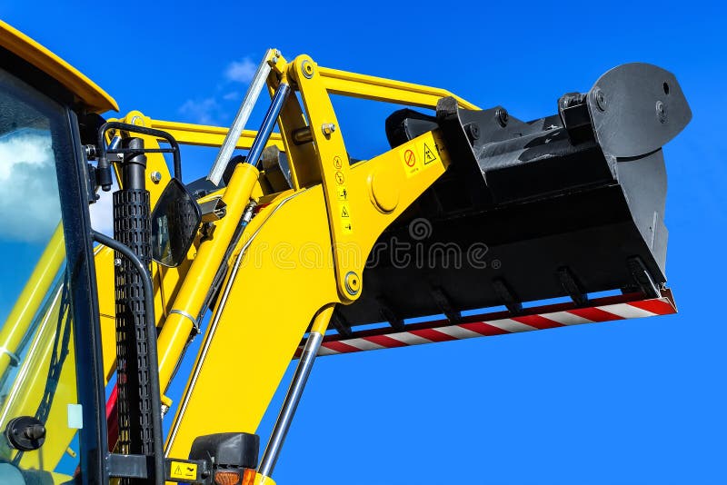 Bright yellow tractor-loader on a background of the clear blue sky, cabin with the lifted ladle close up. Bright yellow tractor-loader on a background of the clear blue sky, cabin with the lifted ladle close up