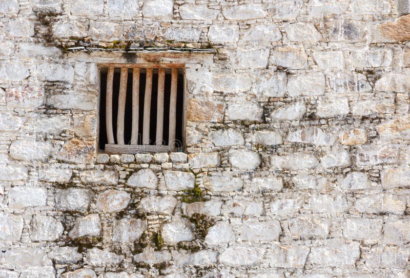 Prison cell window with wooden bars in a white brick wall