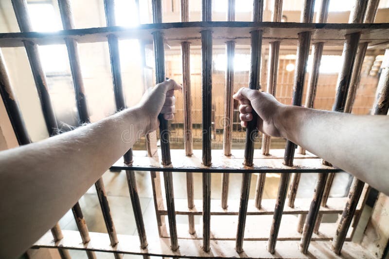 Prisoner man in jail holding hand in prison cell grid.