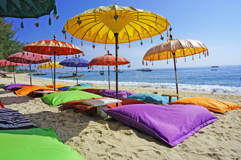 L'immagine mostra alcuni colorati ombrelloni e sabbia cuscini in un ambiente tropicale, spiaggia bagnata dal mare di Bali.