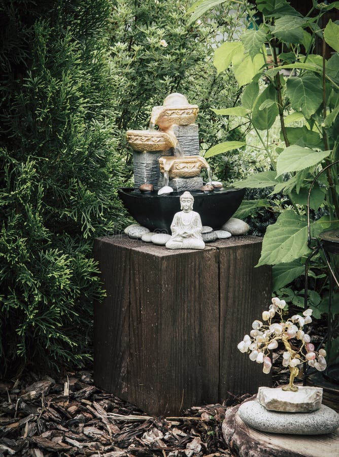 Privater Brunnen des kleinen Hausgartens mit meditierender Buddha-Statue zwischen Bäumen und Büschen. stockfotos