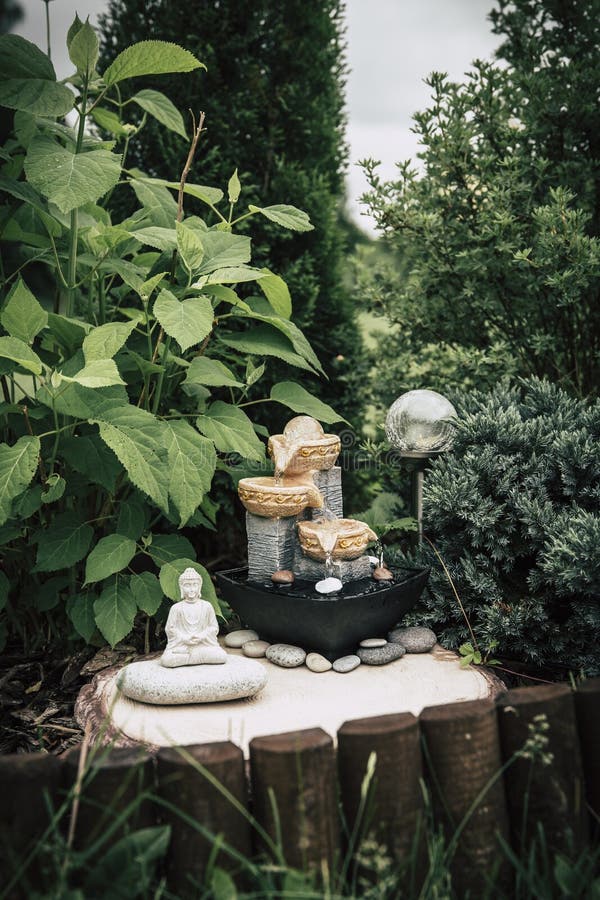 Privater Brunnen des kleinen Hausgartens mit meditierender Buddha-Statue zwischen Bäumen und Büschen. stockfoto