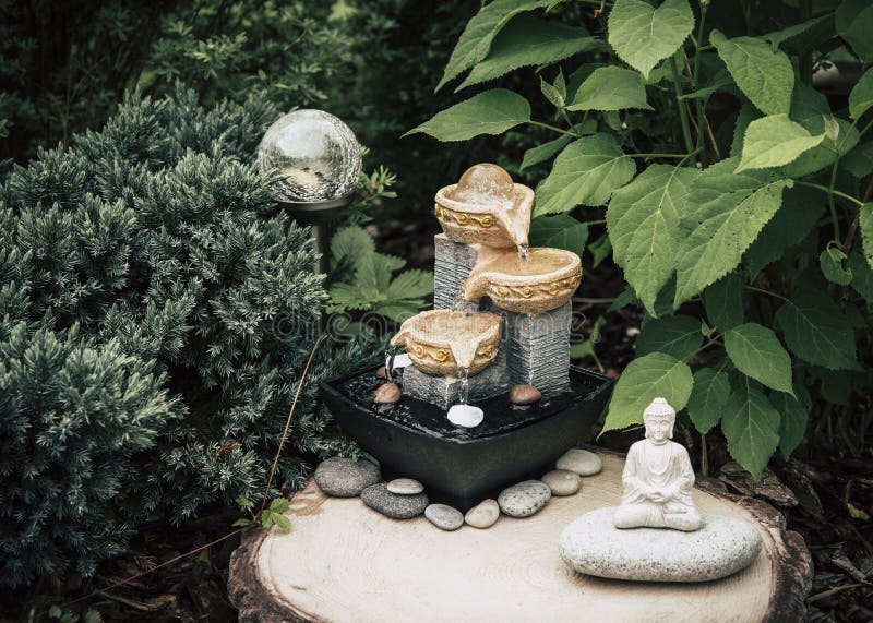 Privater Brunnen des kleinen Hausgartens mit meditierender Buddha-Statue zwischen Bäumen und Büschen. stockbilder