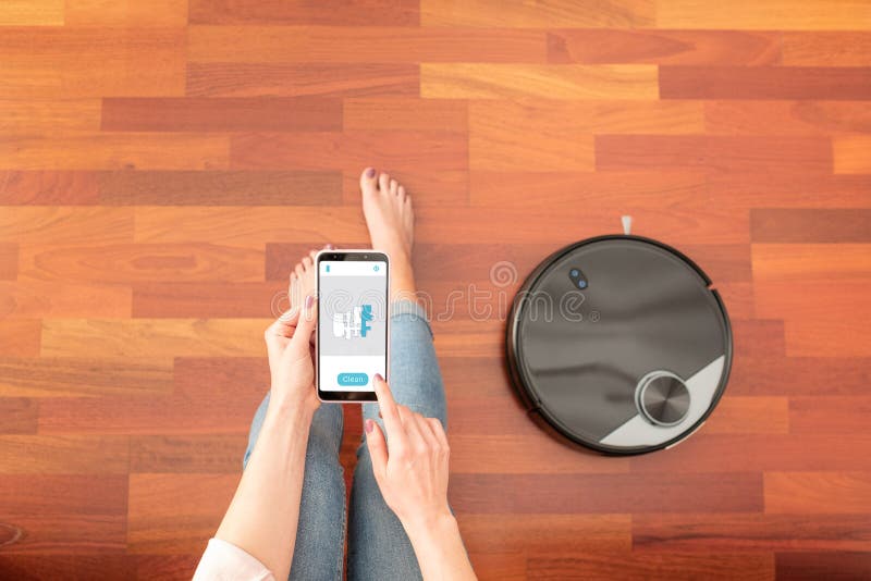 Priveliștea de sus a unei fete fără chip din mijloc care folosește un telefon inteligent pentru a controla un aspirator automat pe stock photo