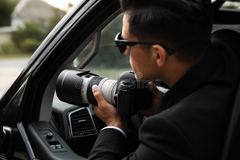 Privédetective met camera die vanuit een auto bespiedt stock foto's