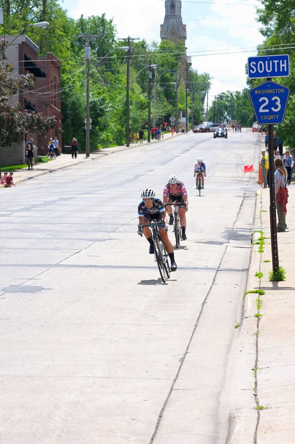 Pro Cyclists at Bottom of Hill in Stillwater. Stillwater, Minnesota, USA - June 15, 2014: Women pro cyclists approach bottom of downhill during final stage of stock photography Pro Cyclists at Bottom of Hill in Stillwater. Stillwater, Minnesota, USA - June 15, 2014: Women pro cyclists approach bottom of downhill during final stage of stock photography