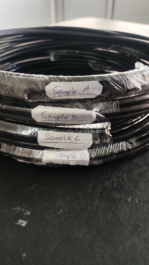 Proben von schwarzen Kabeln in einem Labor. Eine Nahansicht schwarzer Kabel, die in Kunststoff verpackt sind. Die Kabel sind mit handgeschriebenen Buchstaben a b c gekennzeichnet und weisen darauf hin, dass es sich um verschiedene Proben für wissenschaftliche Versuche oder Analysen in Laborbedingungen handelt..