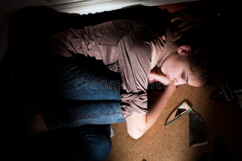 Teenage problems. lonely, unhappy, sad girl lying on the dirty floor in a dark room. Hard selective light. Teenage problems. lonely, unhappy, sad girl lying on the dirty floor in a dark room. Hard selective light.