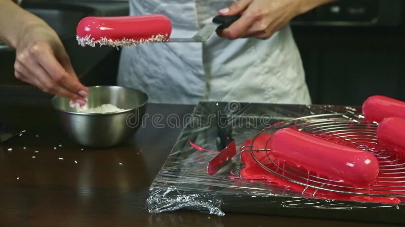 Proceso de decorar el eclair de acristalamiento rosa ovalado con afeitado de coco por confitería