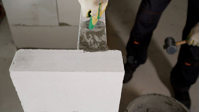 The process of building a wall of blocks. An industrial mason worker installs masonry on a wall with a rubber mallet. A stock photography