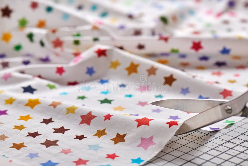 Process cutting fabric with a pattern of colorful stars by scissors on craft mat