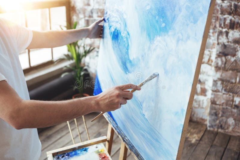 Process of drawing an artist work in art loft studio with oilpaints. Painter hold paintbrush in hand in front of canvas on easel stock photography Process of drawing an artist work in art loft studio with oilpaints. Painter hold paintbrush in hand in front of canvas on easel stock photography