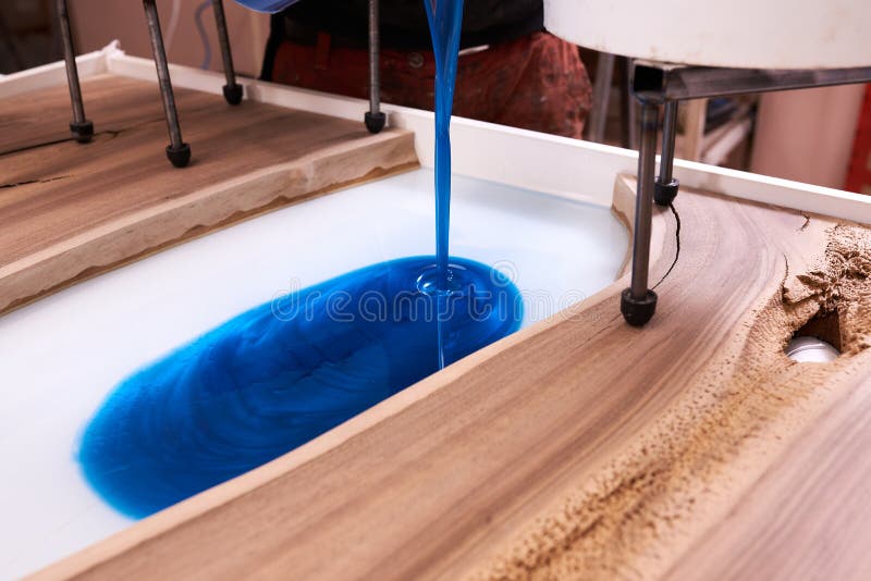Process making of a craft resin and wood table. Liquid epoxy is poured into a mold with wooden blanks stock images
