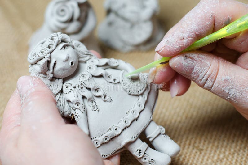 The process of making a souvenir doll made of clay. Female hands holding a toy made of clay.