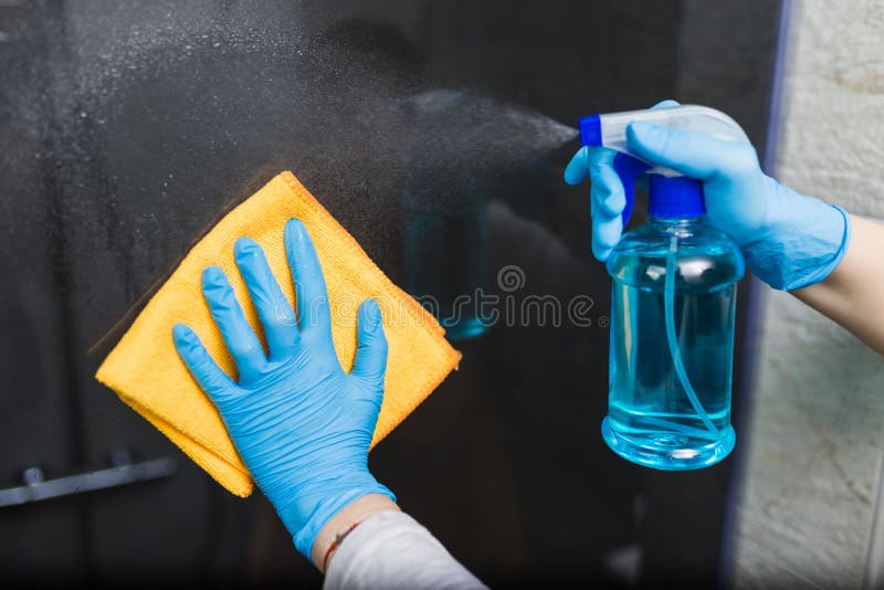 Close up of female hands in rubber gloves cleaning shower cabin glass with microfiber cloth and spray disinfectant. Close up of female hands in rubber gloves cleaning shower cabin glass with microfiber cloth and spray disinfectant