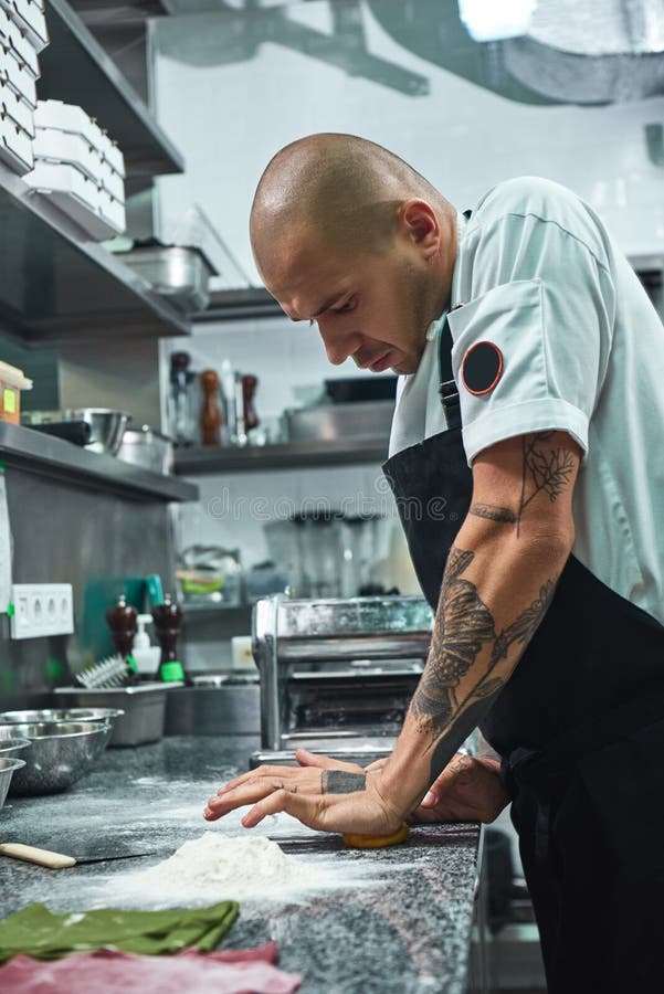 Processus fonctionnant Photo verticale du chef professionnel beau avec des tatouages sur ses mains malaxant la pâte dans le resta photo stock Processus fonctionnant Photo verticale du chef professionnel beau avec des tatouages sur ses mains malaxant la pâte dans le resta photo stock