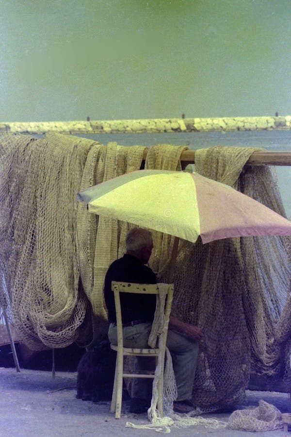 PROCIDA, WŁOCHY, 1975 - rybak naprawia jego sieci rybackie na molu w cieniu parasol obraz royalty free PROCIDA, WŁOCHY, 1975 - rybak naprawia jego sieci rybackie na molu w cieniu parasol obraz royalty free