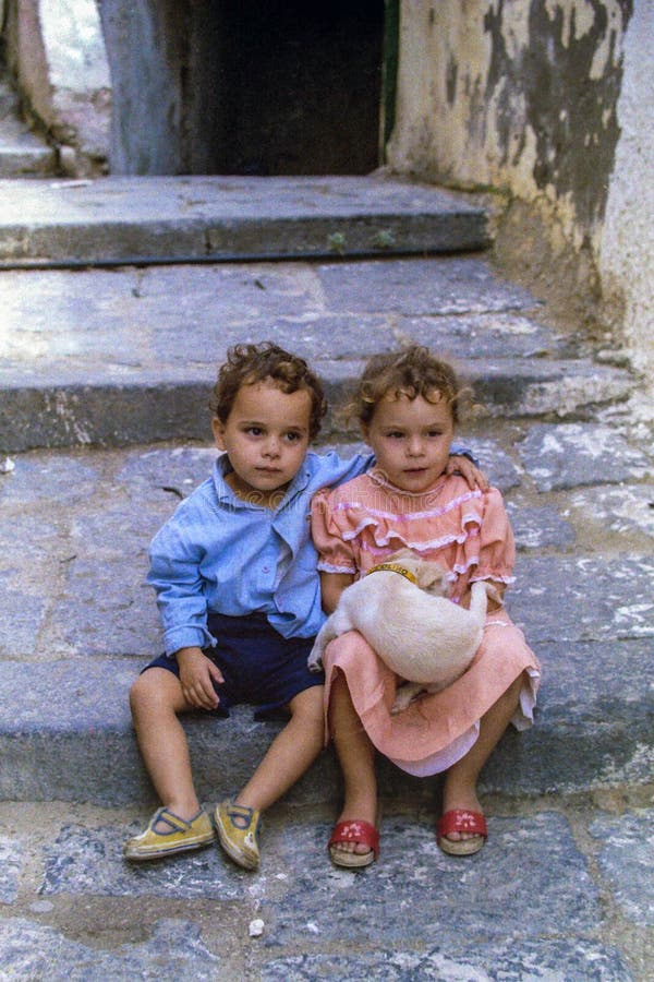 PROCIDA, ITALY, 1978 - A child with his arm lovingly protects his sister who is holding a little dog on her lap. PROCIDA, ITALY, 1978 - A child with his arm lovingly protects his sister who is holding a little dog on her lap.