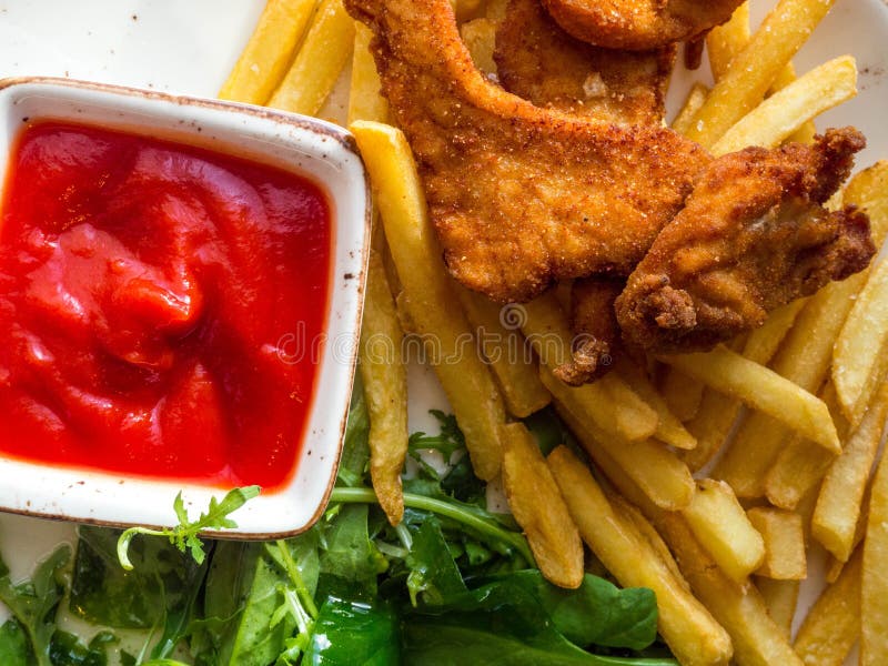 Prodotti degli alimenti a rapida preparazione: patate fritte e pepite di pollo sulla tavola di legno, salsa al pomodoro, verdi fotografie stock Prodotti degli alimenti a rapida preparazione: patate fritte e pepite di pollo sulla tavola di legno, salsa al pomodoro, verdi fotografie stock