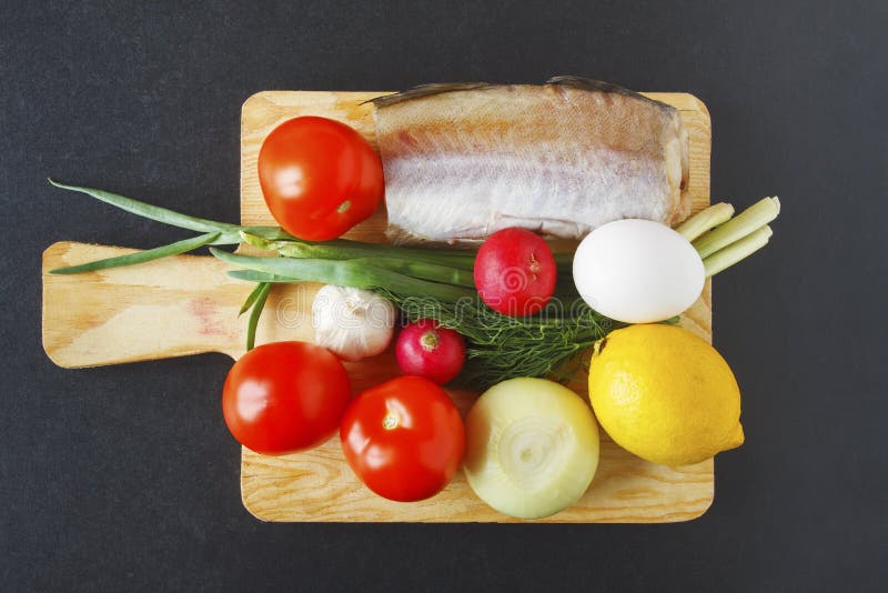 Product set for healthy balanced dish on black background. Fresh organic vegetables and fish piece on cutting board. Top view.