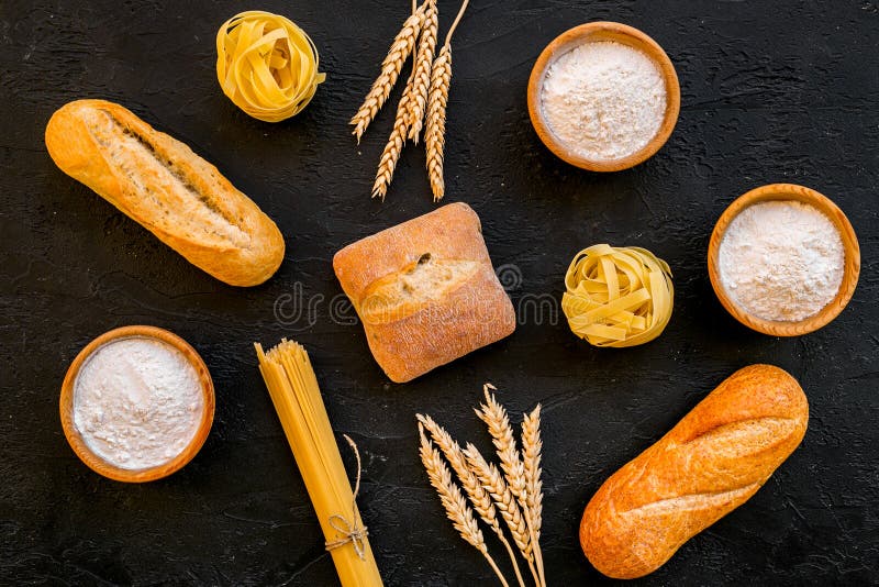 Products made of wheat flour. White flour in bowl, wheat ears, fresh bread and raw pasta on black background top view