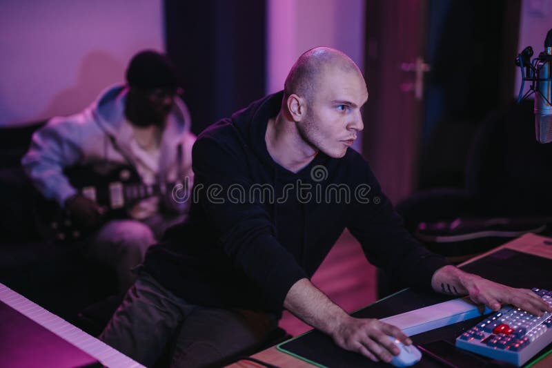 Producător muzical concentrat care lucrează într-un studio de înregistrări cu chitarist în fundal stock photography