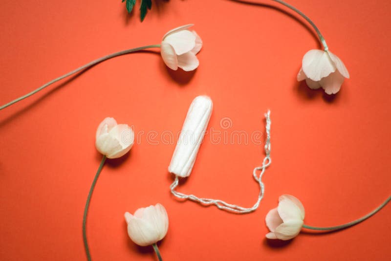Produkty higieniczne dla kobiet na pomaraÅ„czowym tle. Tampon samicy otoczony kwiatami na tle koralowym zdjęcie royalty free Produkty higieniczne dla kobiet na pomaraÅ„czowym tle. Tampon samicy otoczony kwiatami na tle koralowym zdjęcie royalty free