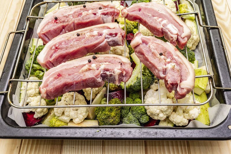 Produtos hortícolas frescos classificados em tabuleiro de cozedura Carne crua de barriga de porco na grelha imagem de stock royalty free Produtos hortícolas frescos classificados em tabuleiro de cozedura Carne crua de barriga de porco na grelha imagem de stock royalty free