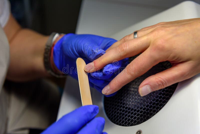 Profesjonalny mistrz manicure w niebieskich rękawiczkach tworzą kształt do paznokci klienta z plikiem do paznokci, zamknij się Na zdjęcie stock Profesjonalny mistrz manicure w niebieskich rękawiczkach tworzą kształt do paznokci klienta z plikiem do paznokci, zamknij się Na zdjęcie stock