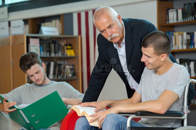 Profesor ayudando a los estudiantes de la biblioteca uno en silla de ruedas fotografía de archivo