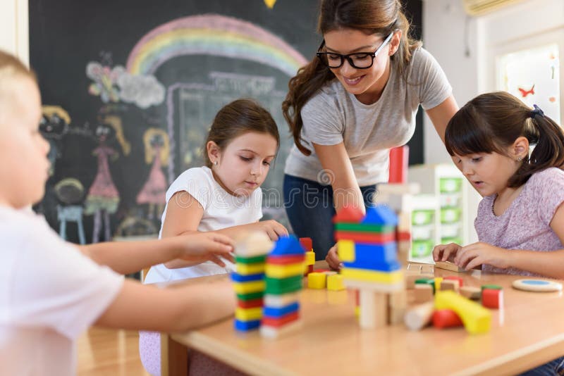 Profesor preescolar con los niños que juegan con los juguetes didácticos de madera coloridos en la guardería foto de archivo libre de regalías Profesor preescolar con los niños que juegan con los juguetes didácticos de madera coloridos en la guardería foto de archivo libre de regalías